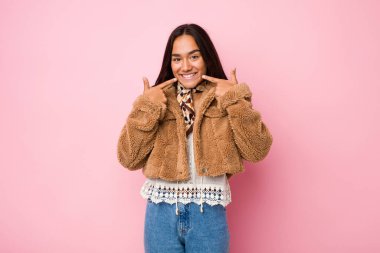 Genç melez Hintli kadın, kısa bir koyun derisi palto giymiş, parmaklarını ağıza doğrultuyor..