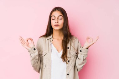 Young caucasian woman posing in a pink background relaxes after hard working day, she is performing yoga.