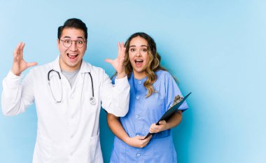 Mavi arka planda poz veren genç doktor çift hoş bir sürprizle karşılaştı, heyecanlandı ve ellerini kaldırdı..