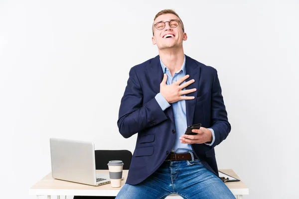 Young business man with a laptop laughs out loudly keeping hand on chest.
