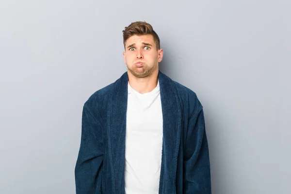 Young Caucasian Man Wearing Pajama Blows Cheeks Has Tired Expression — ストック写真