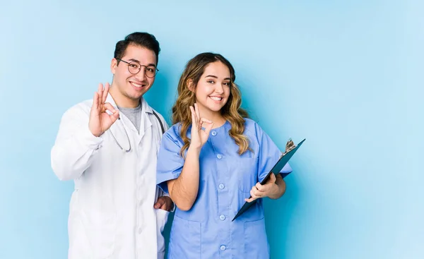 Joven Pareja Médicos Posando Fondo Azul Aislado Alegre Confiado Mostrando —  Fotos de Stock