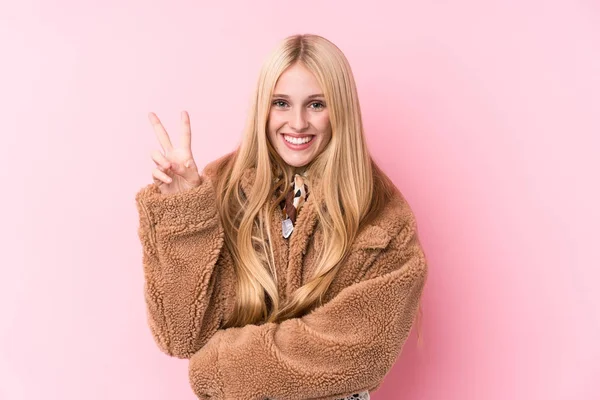 年轻的金发女人穿着一件粉色背景的外套 手指头是二号 — 图库照片