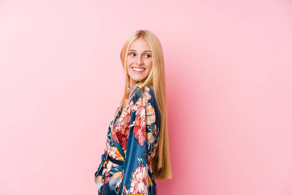Young blonde woman wearing a kimono pajama looks aside smiling, cheerful and pleasant.