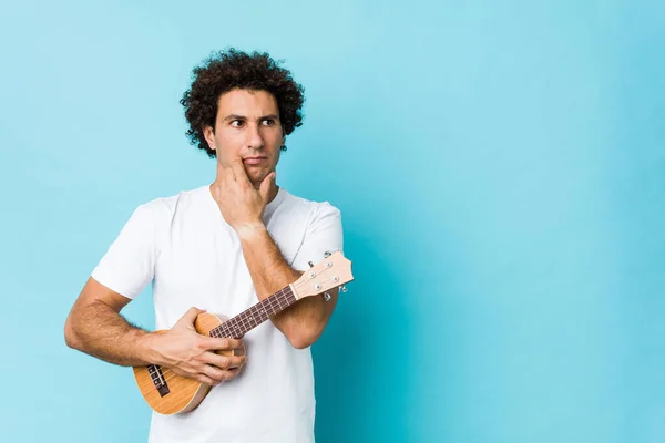 Young Caucasian Curly Man Playing Ukelele Relaxed Thinking Something Looking — Stock Photo, Image