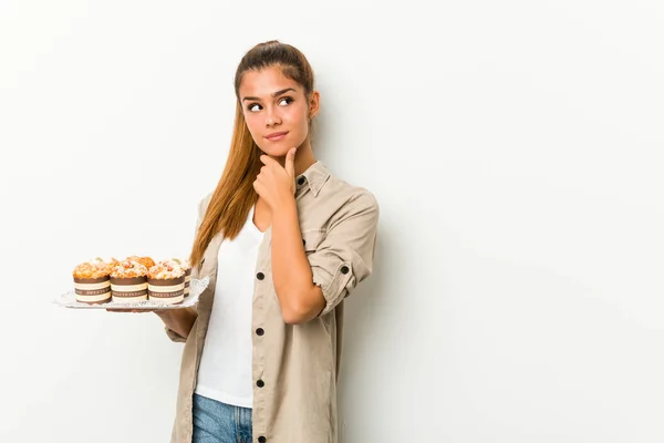 Young Caucasian Woman Holding Sweet Cakes Looking Sideways Doubtful Skeptical — Stock Photo, Image