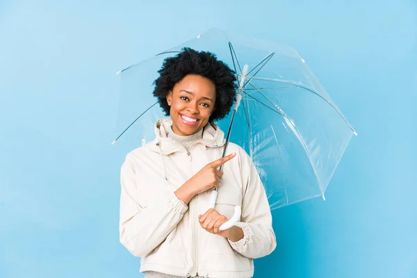若いアフリカ系アメリカ人の女性が傘を差して笑顔を見せながら脇を指差して — ストック写真