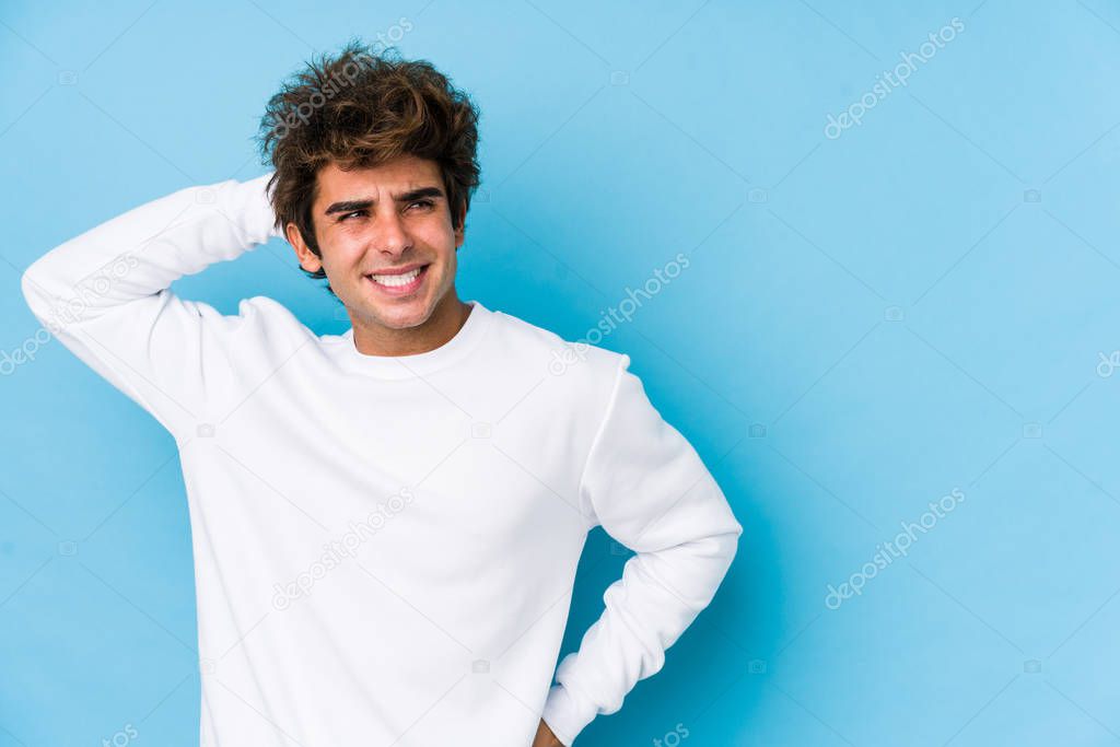 Young caucasian man against a blue background isolated touching back of head, thinking and making a choice.