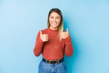 Kafkasyalı genç bir kadın yalnız poz veriyor. Baş parmağını kaldırıyor, gülümsüyor ve kendinden emin..