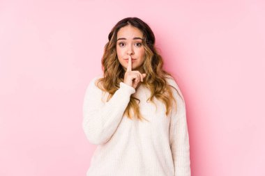 Pembe arka planda poz veren kıvrımlı genç bir kadın bir sır saklıyor ya da sessizlik istiyor..