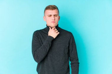 Mavi arka plandaki genç beyaz adam virüs ya da enfeksiyon yüzünden boğaz ağrısı çekiyor..