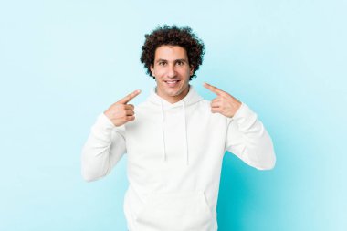 Mavi arka planda genç bir sporcu gülümsüyor, parmaklarını ağıza doğrultuyor..