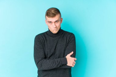 Mavi arka planda beyaz bir adam hoşnutsuzca kaşlarını çatıyor, kollarını kavuşturuyor..