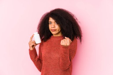 Vitaminlerini tutan genç afro kadın kameraya yumruğunu gösteren vitamini tutan genç afro kadın, agresif yüz ifadesi..