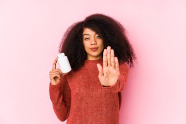 Vitaminlerini tutan genç bir afro kadın vitamini tutan ve elini uzatarak dur işaretini gösteren genç bir afro kadın seni engelliyor..