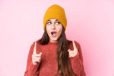 Young caucasian woman wearing a wool cap pointing upside with opened mouth.
