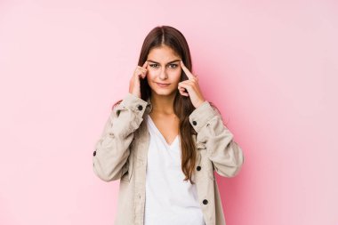 Young caucasian woman posing in a pink background focused on a task, keeping forefingers pointing head.