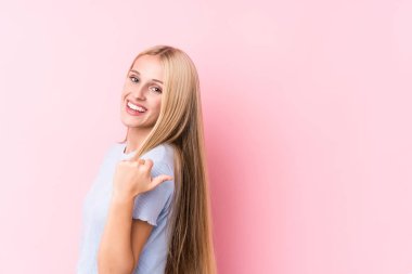 Pembe arka plandaki genç sarışın kadın başparmak uzakta, gülüyor ve kaygısız..
