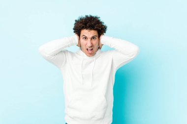 Genç sporcu, mavi arka planda kulakları kulaklarıyla kapatıyor ve yüksek ses duymamaya çalışıyor..