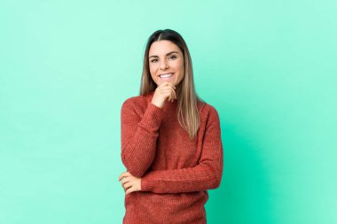 Kafkasyalı genç bir kadın yalnız, mutlu ve kendinden emin gülümsüyor, elleriyle çenesine dokunuyor..