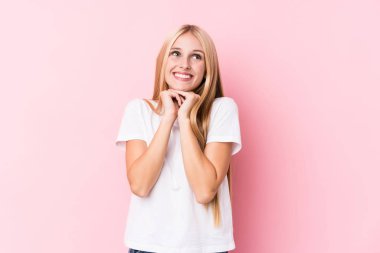 Pembe arka plandaki genç sarışın kadın ellerini çenesinin altında tutuyor ve mutlu bir şekilde yan tarafa bakıyor..