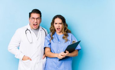 Mavi arka planda poz veren genç bir doktor çift çok sinirli ve agresif çığlıklar atıyor..