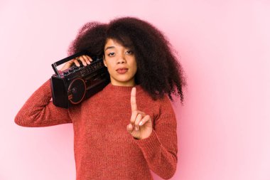 Elinde bir kaset tutan genç bir afro kadın bir numarayı parmağıyla gösteriyor..