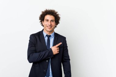 Genç iş adamı beyaz arka planda gülümseyen ve bir kenara işaret eden, boş alanda bir şey gösteren kıvırcık saçlı adam..
