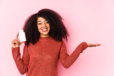 Vitaminlerini tutan genç afro kadın avucunun içinde fotokopi alanı gösteren vitaminlerle izole edilmiş genç bir afro kadın ve belinden bir el daha tutuyor..