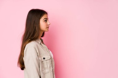 Young caucasian woman posing in a pink background gazing left, sideways pose.
