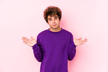 Pembe arka planda genç beyaz bir adam şüpheli ve omuz silkiyor..