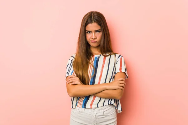 Young slim woman frowning face in displeasure, keeps arms folded.