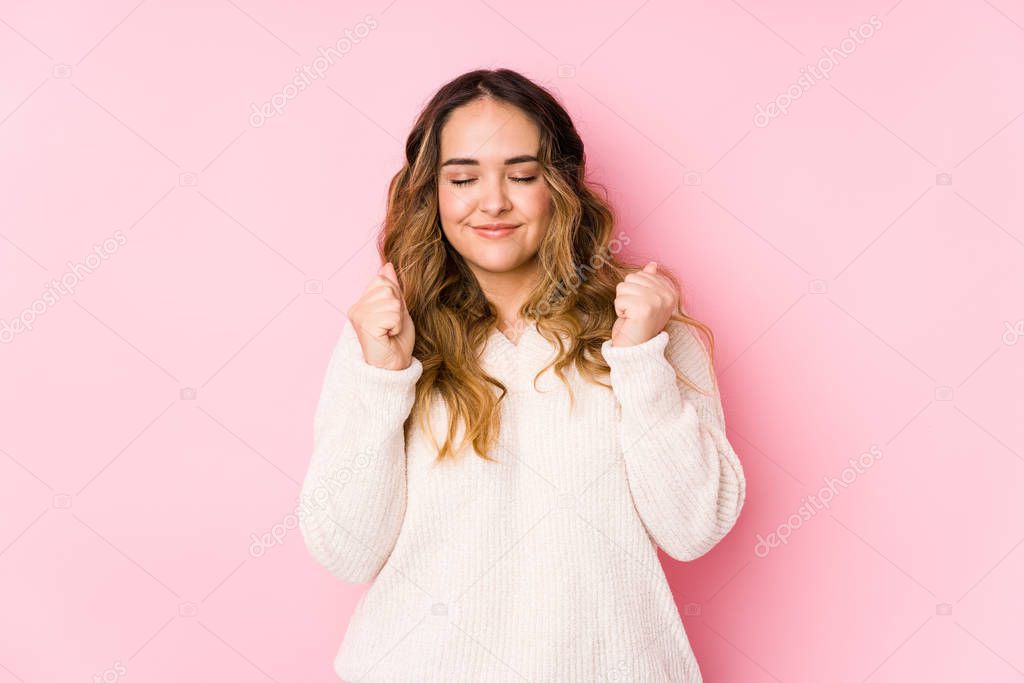 Young curvy woman posing in a pink background isolated raising fist, feeling happy and successful. Victory concept.