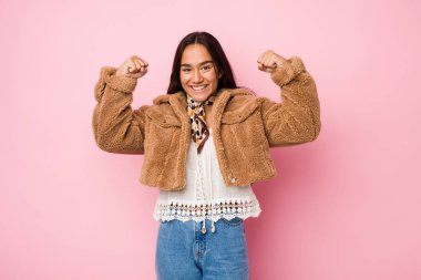 Genç melez Hintli kadın kısa bir koyun derisi ceket giyiyor. Güçlü hareketlerini kollarıyla gösteriyor. Kadınsı gücün sembolü.