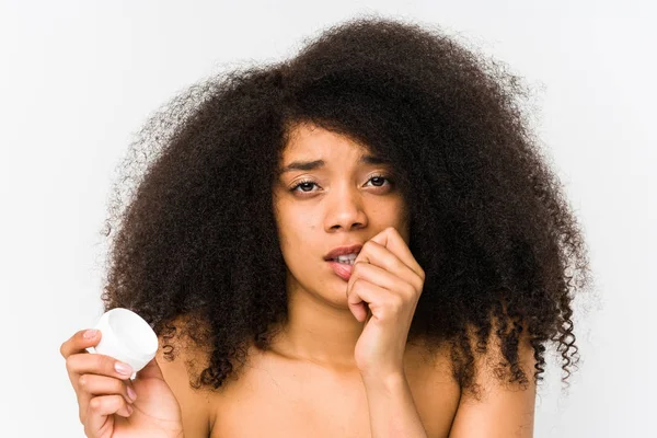 Mujer Afro Joven Sosteniendo Una Crema Hidratante Aislada Mordiendo Las — Foto de Stock