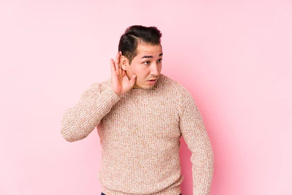 Νεαρός Καμπυλωτός Άντρας Ποζάρει Ροζ Φόντο Απομονωμένος Προσπαθώντας Ακούσει Ένα — Φωτογραφία Αρχείου