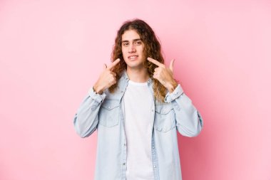 Uzun saçlı adam münzevi gülümsemeler sergiliyor, parmaklarını ağıza doğrultuyor..