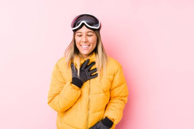 Pembe arka planda kayak kıyafeti giyen beyaz bir kadın elini göğsüne koyduğunda kahkahalar atıyor..