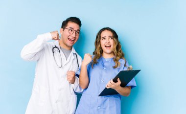 Mavi arka planda poz veren genç doktor çift zaferden sonra yumruklarını kaldırıyor..