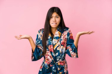 Kimono pijama giyen Asyalı genç bir kadın kopya alanı tutmak için omuz silkiyor ve kafası karışık..