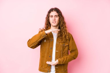 Genç, uzun saçlı bir adam poz veriyor. Elinde iki eliyle bir şey tutuyor..