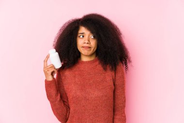 Vitaminlerini tutan genç afro bir kadın vitamini karıştıran genç bir afro kadın, şüpheli ve güvensiz hissediyor..