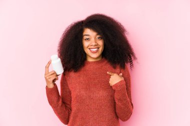 Vitaminlerini tutan genç afro kadın elinde vitaminsperson ile gururlu ve kendinden emin bir şekilde bir gömlek fotokopisini işaret ediyor.