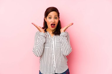 Orta yaşlı Latin bir kadın. Pembe arka planda izole edilmiş. Şaşırmış ve şok olmuş..