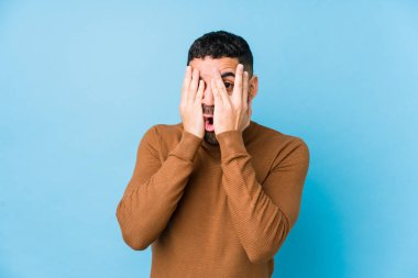 Mavi arka planda genç bir latin adam yalnız, korkmuş ve gergin parmaklarıyla göz kırp..