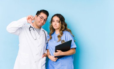 Mavi arka planda poz veren genç bir doktor çift hoşlanmadıkları bir jesti gösteriyor, başparmakları aşağıda. Anlaşmazlık konsepti.