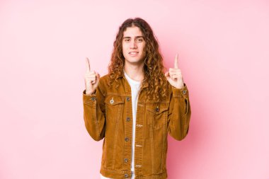 Genç, uzun saçlı, izole bir şekilde poz veren adam, iki ön parmağı da havada, boş bir alan gösteriyor..