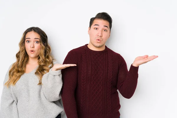 Casal Jovem Posando Fundo Branco Impressionado Segurando Espaço Cópia Palma — Fotografia de Stock