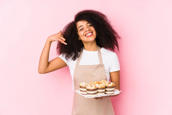 Stock image Young afro pastry maker woman holding a cupcakes isolatedYoung afro baker woman showing a mobile phone call gesture with fingers.