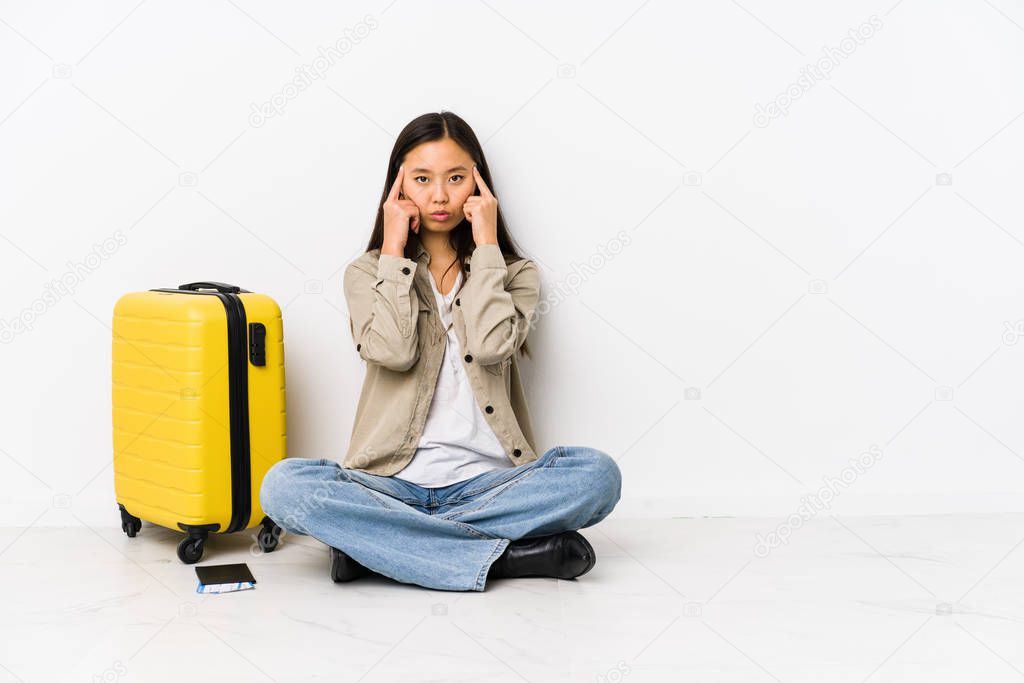 Young chinese traveler woman sitting holding a boarding passes focused on a task, keeping forefingers pointing head.